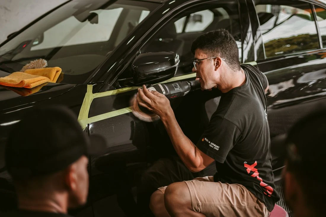A detailer carefully machine-polishing a masked section of a dark car door
