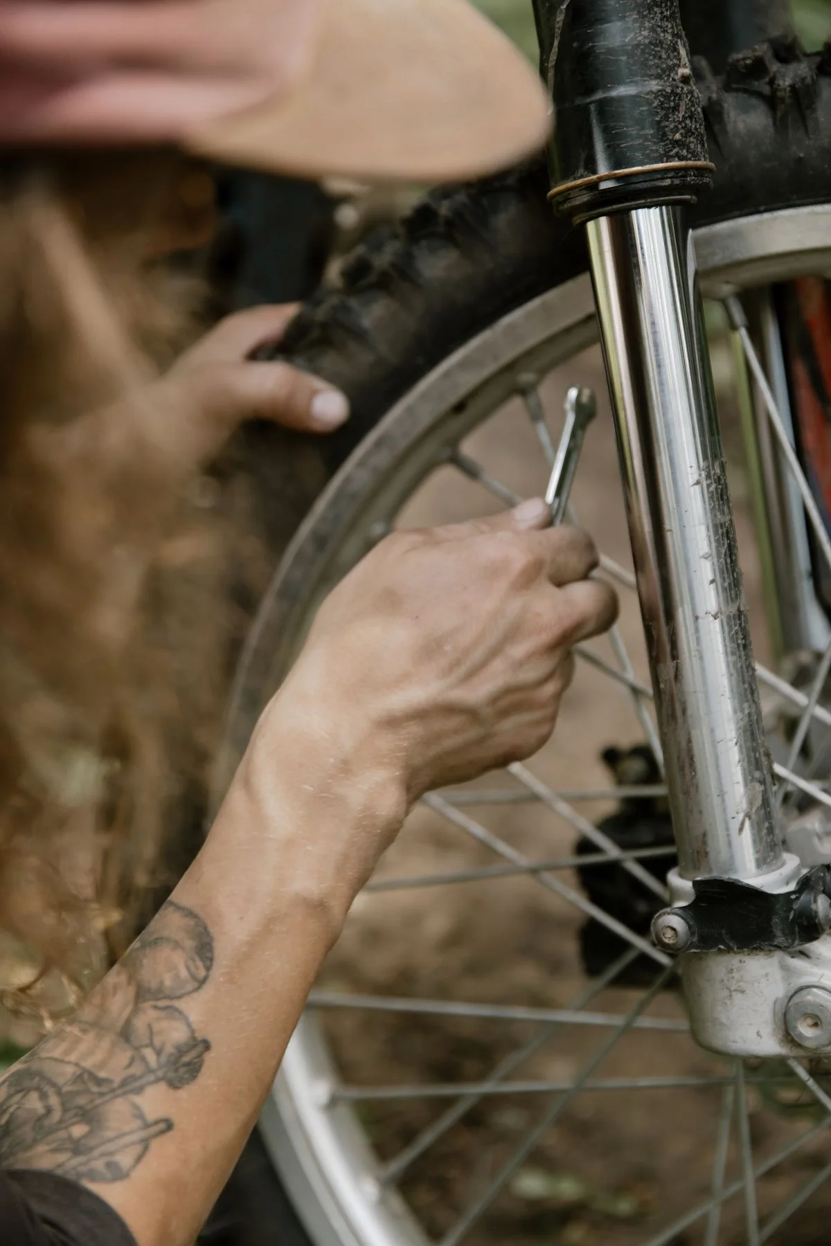 Hands working with a tool beside a bicycle wheel, spokes and front fork