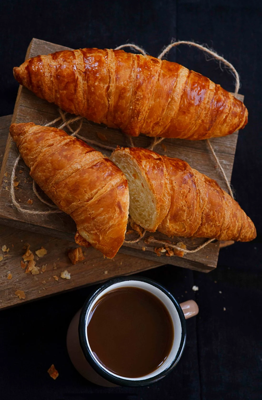 Two croissants on a wooden board with coffee, showing the baked pastry layers
