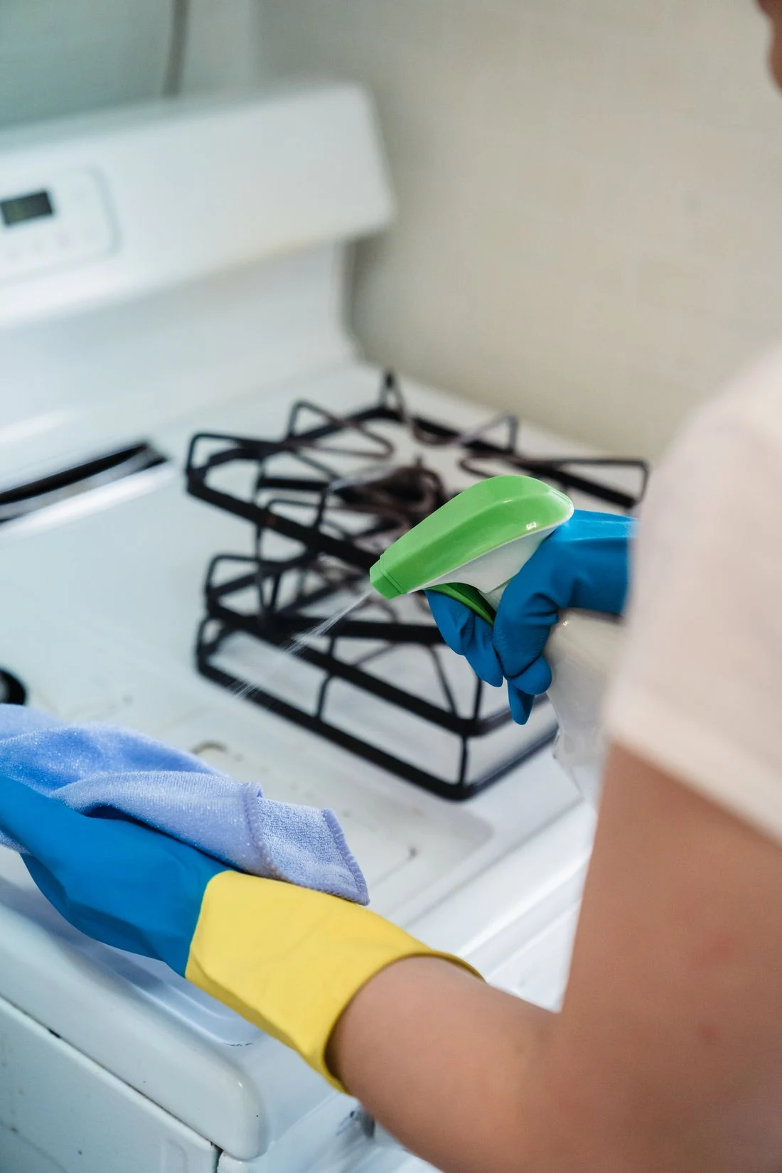 Gloved hands preparing a cleaning cloth and spray beside a kitchen cooker