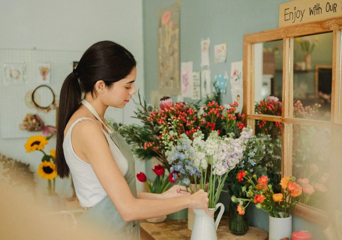 A florist arranging loose stems by hand at a flower-filled workbench