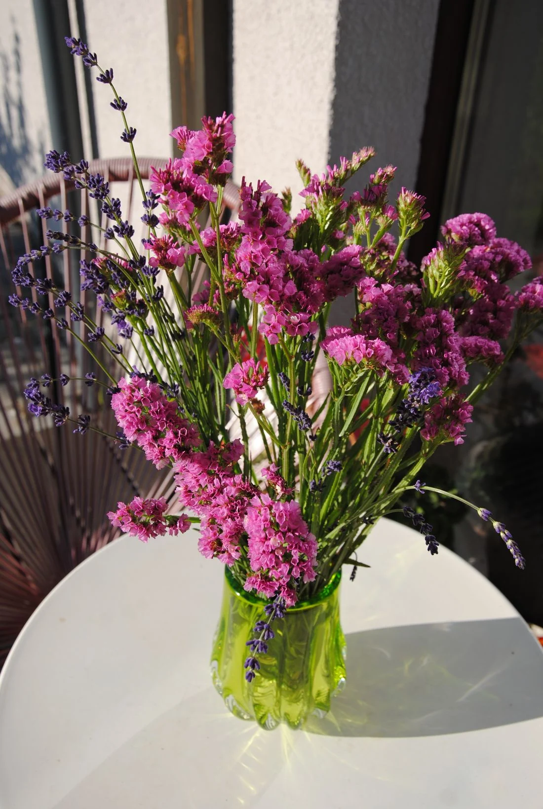 Tall loose purple and pink flowering stems in a green glass vase