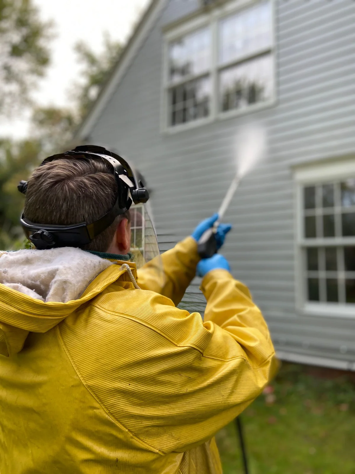 Person in a yellow raincoat directing a cleaning spray at residential exterior cladding